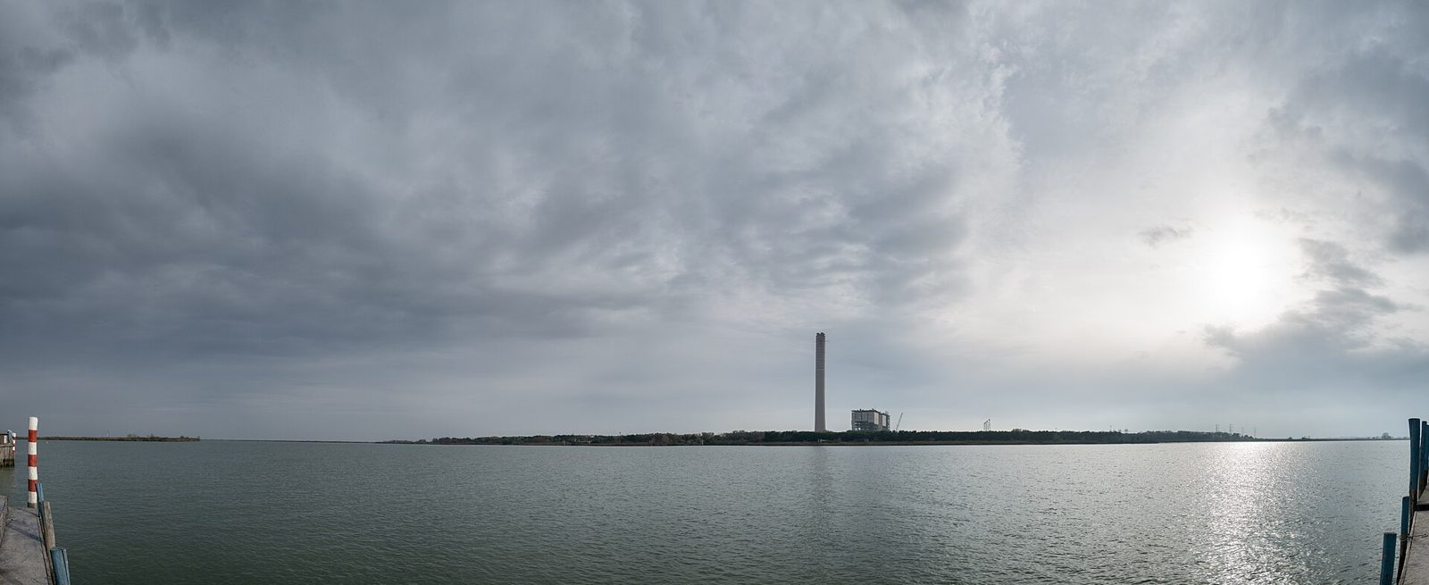 Il Po di Pila sotto un cielo nuvoloso, con la riva lontana e una ciminiera